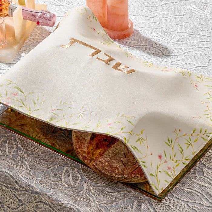 Floral Bird Challah Cover in cream with embroidered design, displayed over a braided loaf on a gray table.