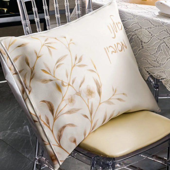 Floral Bird Pesach Set in gold and white leather with embroidered botanical details, displayed on chair with coordinating pillow