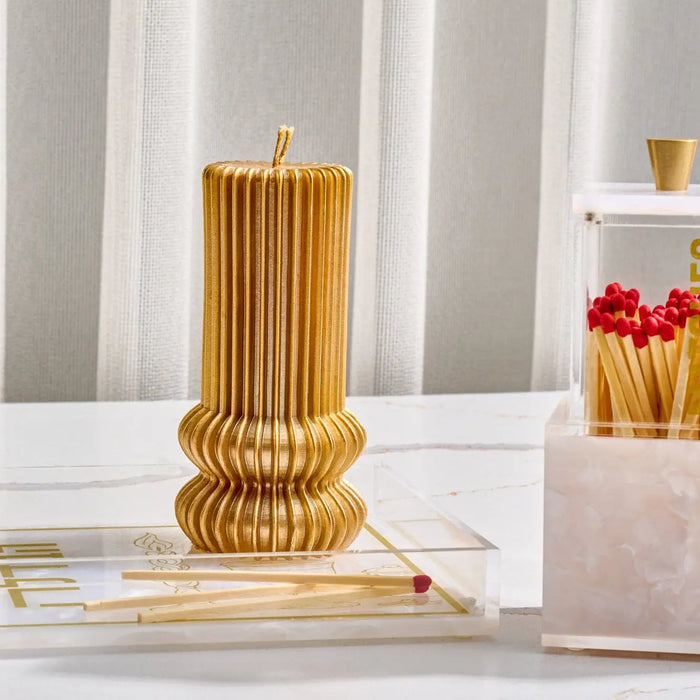 Gold fluted Havdalah candle with ridged texture standing upright on white surface, surrounded by wooden matches in holder.