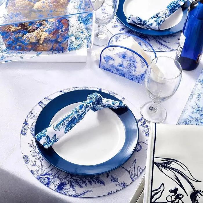 Blue and white French toile napkin displayed on a place setting with matching dinnerware and glassware in a table setting.