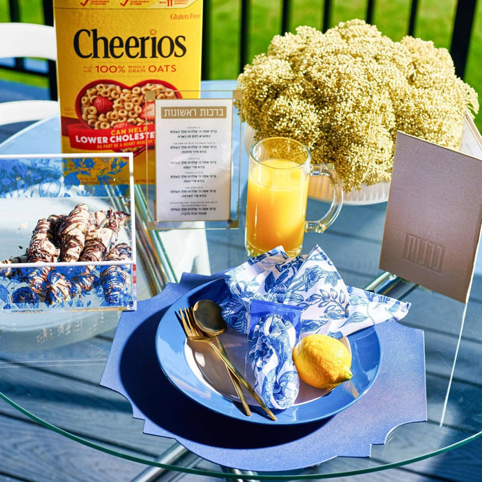 Blue French toile napkin displayed on a place setting with flowers and morning breakfast items on a table.
