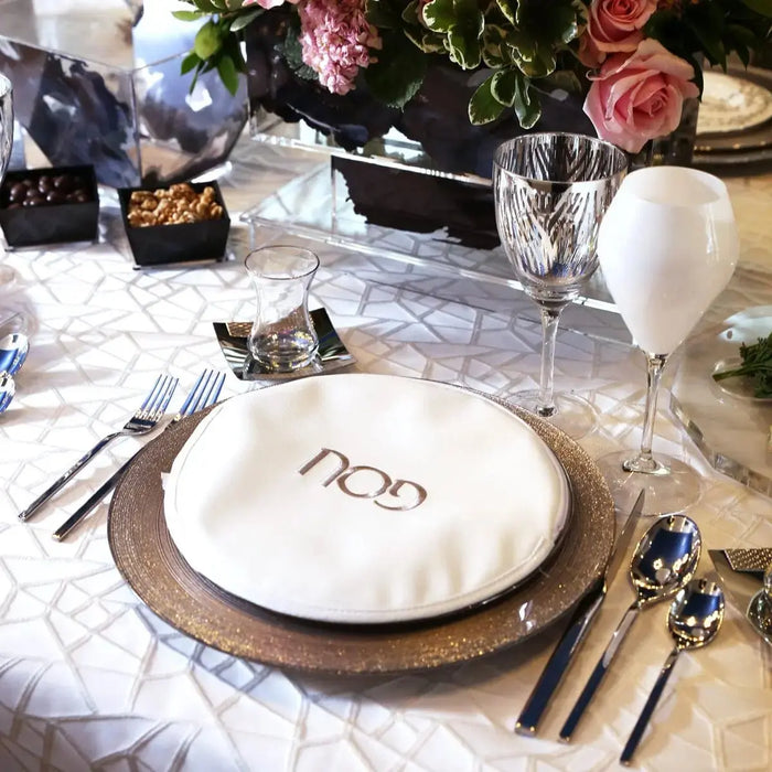Gold leather Gebrochts Matzah Pouch displayed on elegant place setting with white plate and formal tableware for Passover.