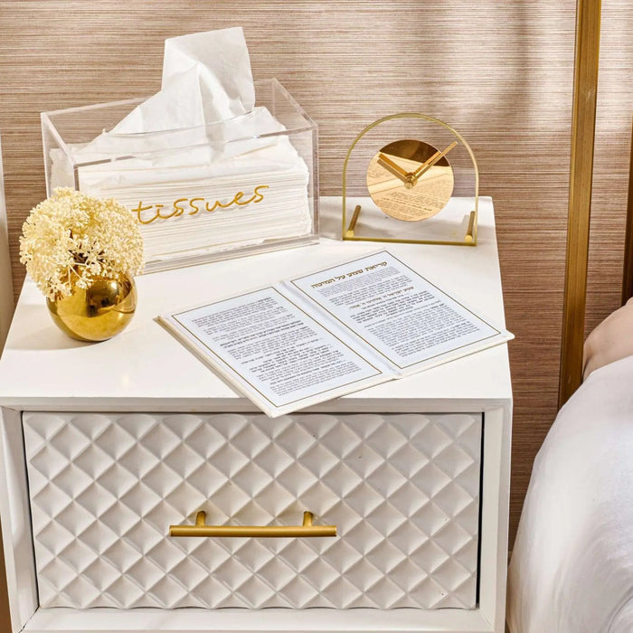 Golden globe faux floral arrangement displayed on white quilted nightstand beside tissue box and decorative items in bedroom setting.