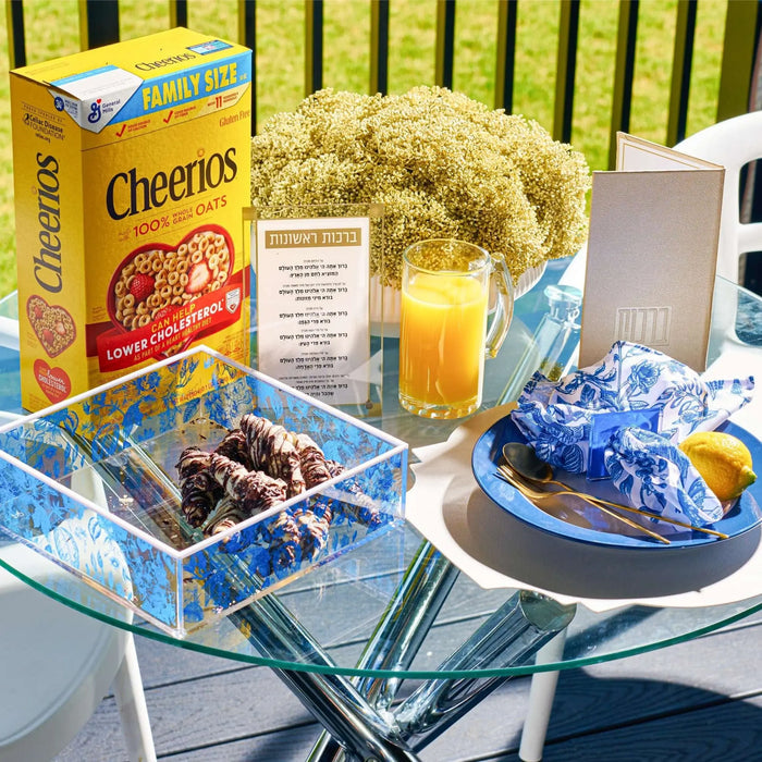 White ceramic flower pot with green faux floral arrangement displayed on table with Cheerios box and juice glass in background.