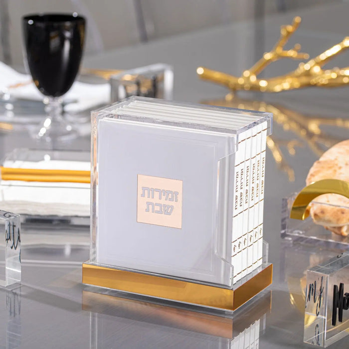 White and gold leather Hardcover Bencher Set with lucite accents, displayed on table with Shabbat candles and religious items.