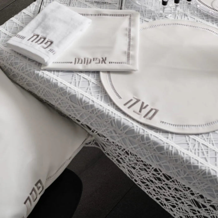 Hemstitched Pesach set with white linen napkins and gray fabric trim, featuring delicate embroidered details and leather accents.