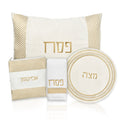 Herringbone Pesach set with cream and gold pieces including pillow cover, matzah cover, plate, and afikoman bag featuring Hebrew text and geometric stripe pattern.