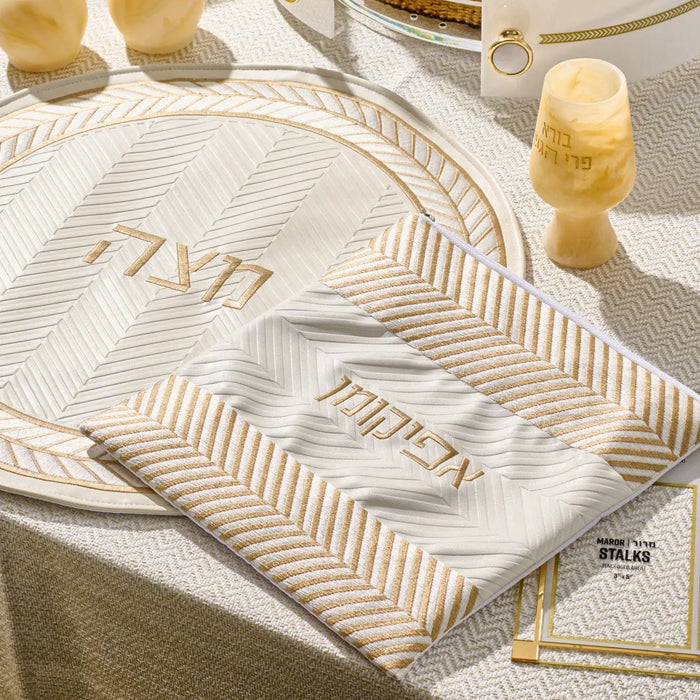 White and gold herringbone afikoman bag with leather details displayed on a place setting during Passover Seder.