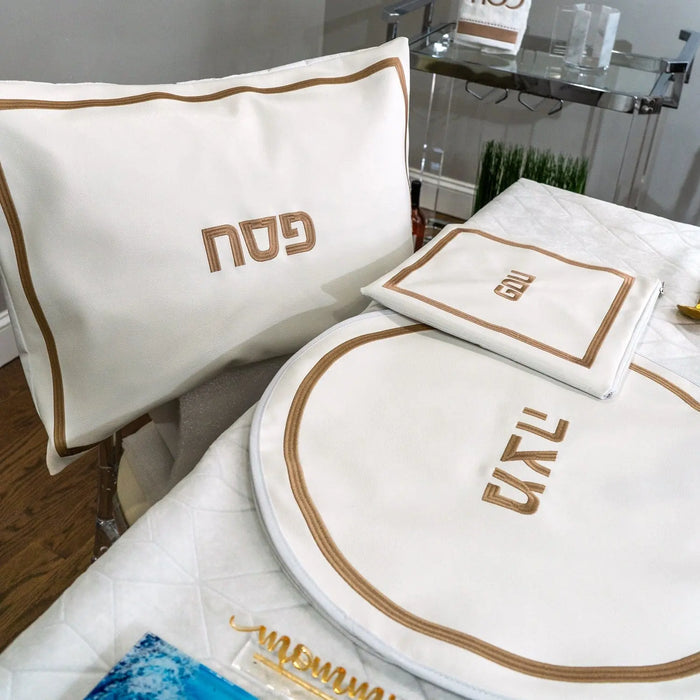 Hotel Style Pesach leather set with cream and tan embroidered details on pillowcase, placemat, and napkin displayed on bed