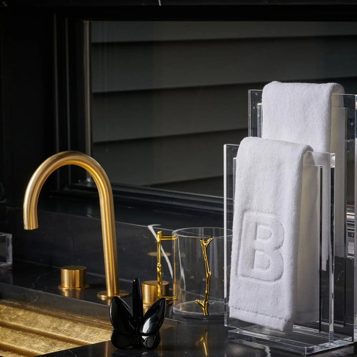 White embossed initial finger towel displayed on vanity counter next to gold faucet and decorative items