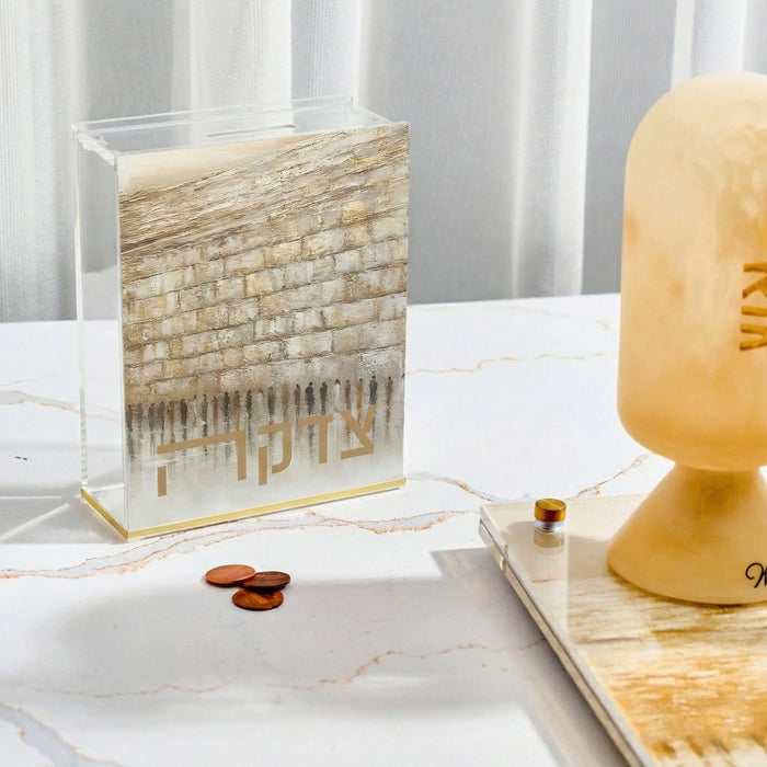 Jerusalem Taupe Tzedakah Box with woven textile design featuring Western Wall imagery, displayed on white surface with candle and home decor.