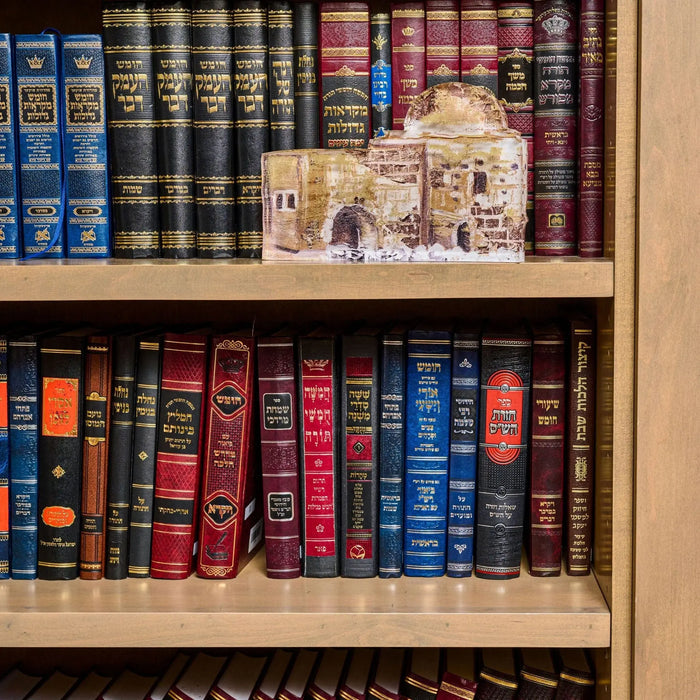 Kever Rochel sculpture displayed on wooden bookshelf with classic books, featuring painted judaica design in cream and gold tones.