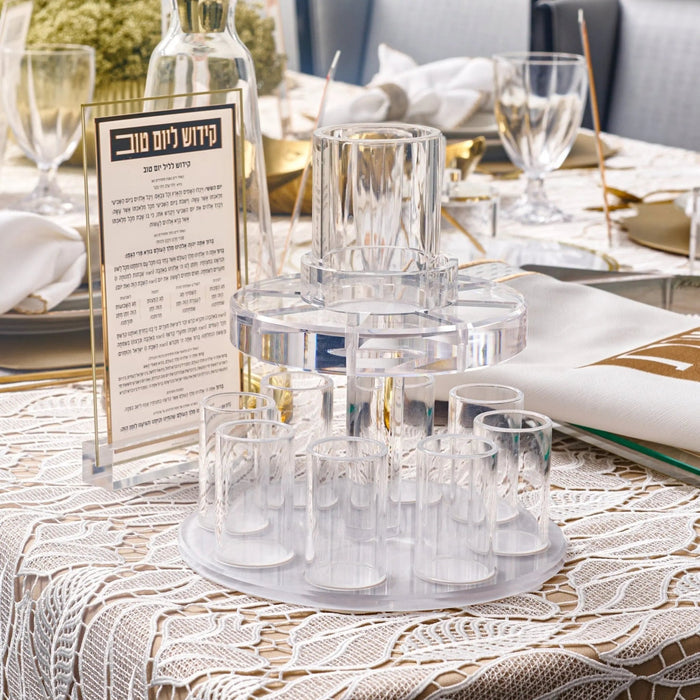 Waterdale Collection glass Kiddush fountain with multiple small cups arranged around a central tower, displayed on a decorated table for Shabbat wine service.