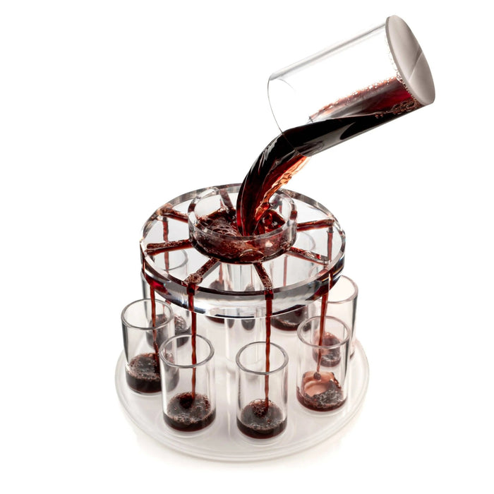 Kiddush fountain with multiple glass cups arranged in a circular metal holder, pouring wine from a tilted bottle at the top.