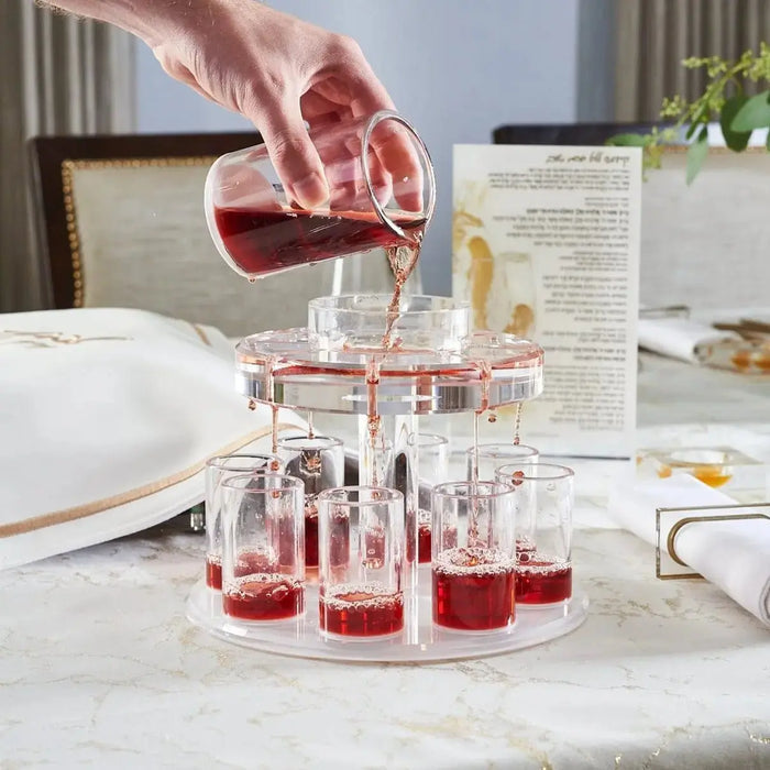 Clear glass Kiddush fountain with red wine in multiple tiers, displayed on marble surface in home setting.