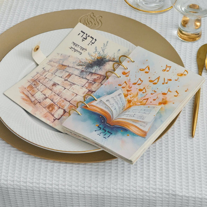 Kids Leather Painted Haggadah in watercolor design, displayed on place setting with gold-rimmed plate and flatware for Pesach celebration.