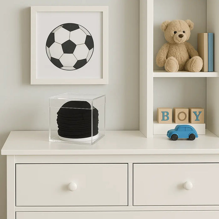 Black cylindrical Kippah Keeper storage container displayed on white dresser with children's room decor and toys nearby.