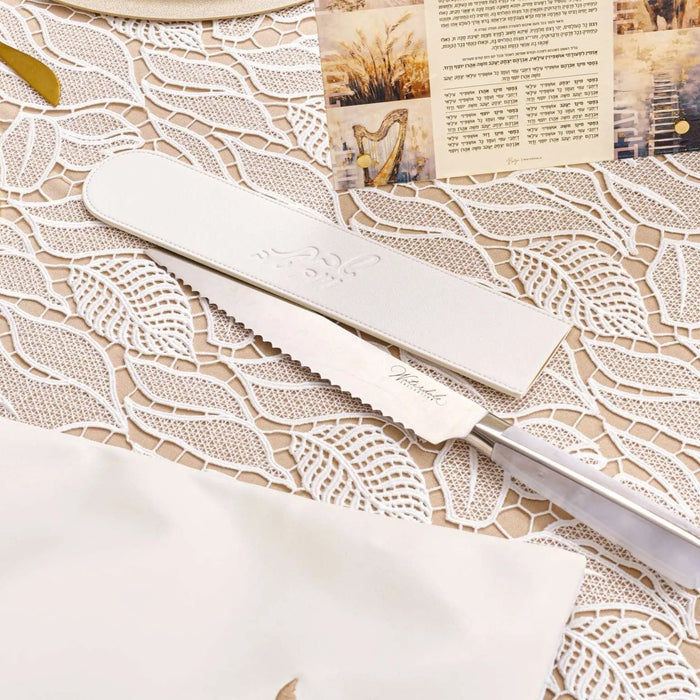 Cream leather knife blade cover displayed on a patterned challah board with dried flowers and newspaper in background.