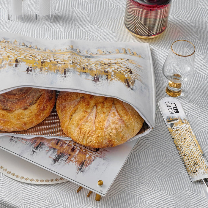 Kosel at Winter painted challah set featuring two golden braided loaves on white ceramic platter with artistic landscape design, displayed with gold accessories.