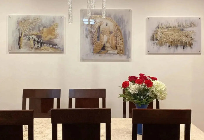 Kosel at Winter painting displayed above wooden dining table with red flowers, showing Jerusalem landscape art in watercolor style framed on wall.