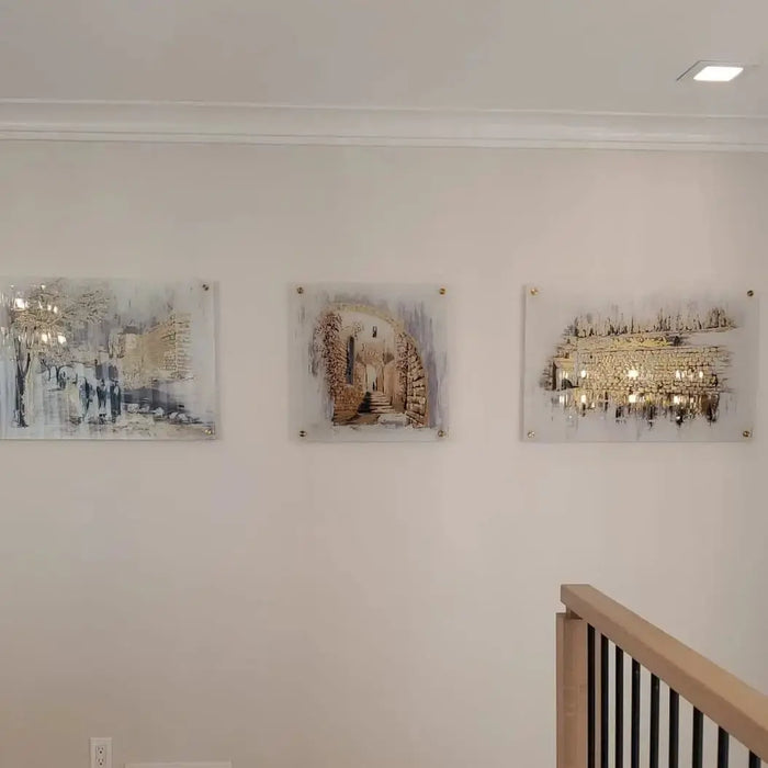 Kosel at Winter painting displayed on white wall above wooden staircase railing, featuring Jerusalem landscape artwork in warm tones.