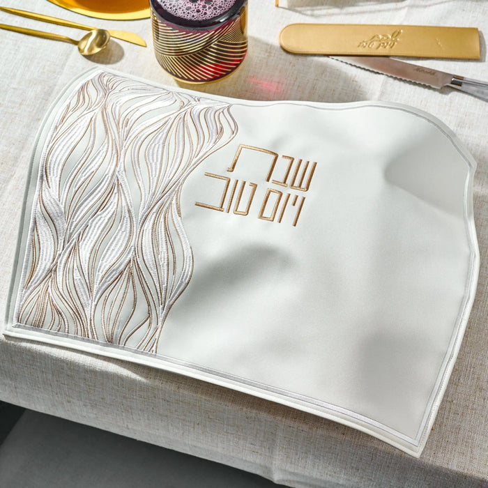 Elegant lace challah cover in gold and white with leather accents, displayed on a table setting for Shabbat.