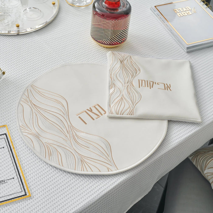 Cream lace matzah cover with delicate floral patterns displayed on a white plate during a Passover table setting.
