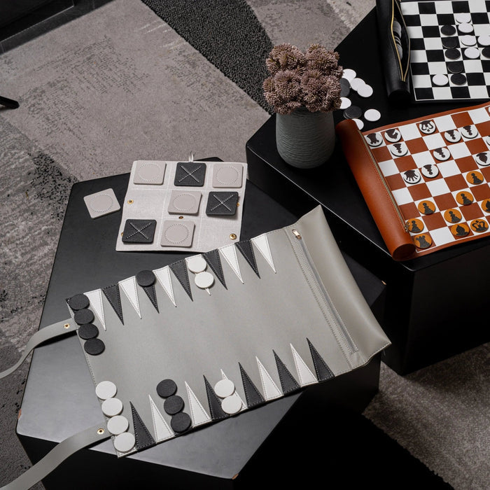 Leather backgammon game with brown case, white playing board, and black and white checkers arranged on surface with dice visible.