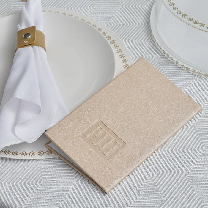 Cream leather bencher with gold accents displayed on white bedding next to a white hand towel and gold bathroom accessory