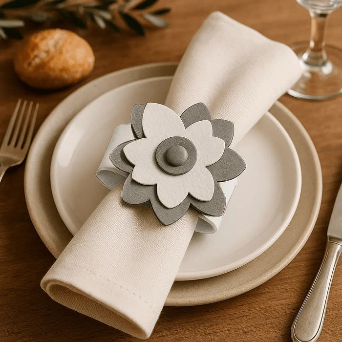 Gray leather flower napkin ring holding a white cloth napkin on a place setting with white plates and wooden table.