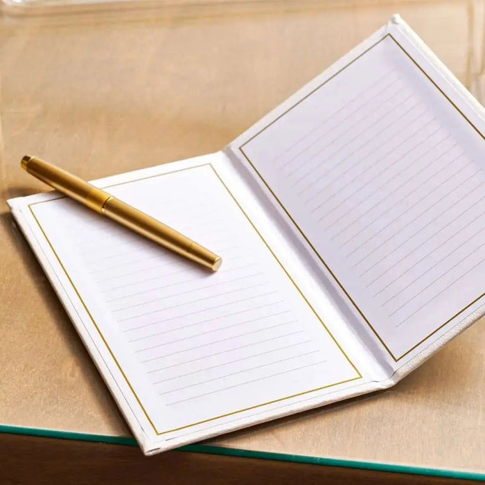Leather gift note booklet in cream with lined pages, shown open next to a closed cover, featuring a gold pen on a wooden surface.