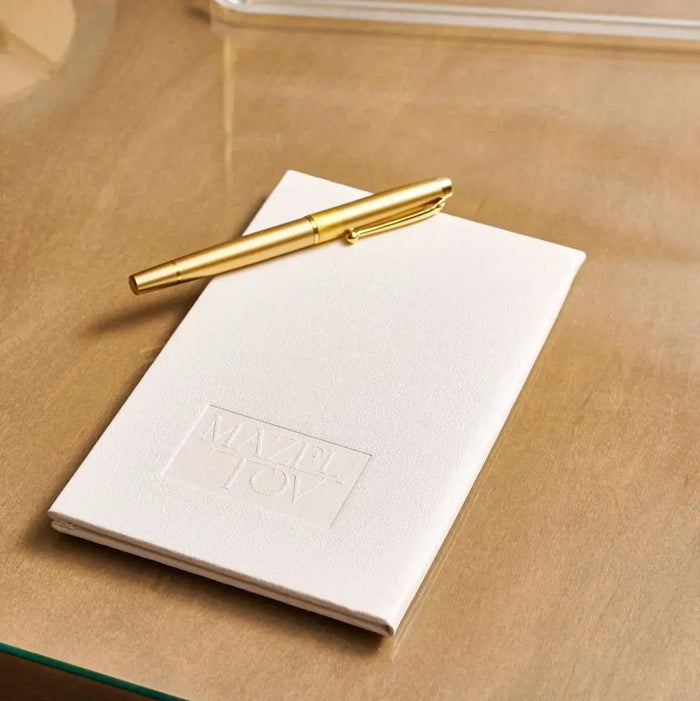 White leather gift note booklet with gold pen on wooden surface, perfect for bat mitzvah cards and thank you notes.