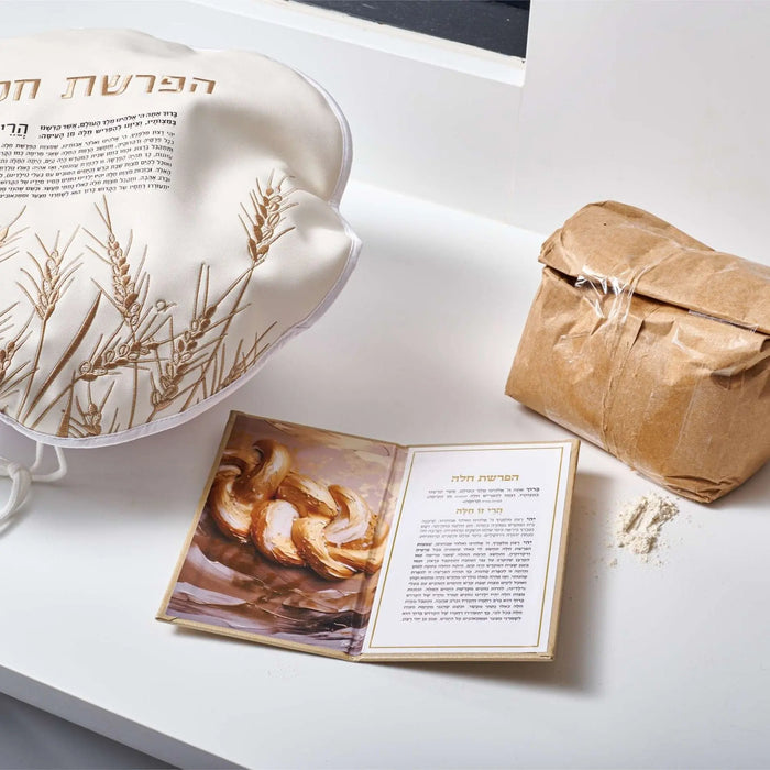 Tan leather Hafrashas Challah booklet displayed with prayer cards, dried flowers, and kraft paper bag on white surface