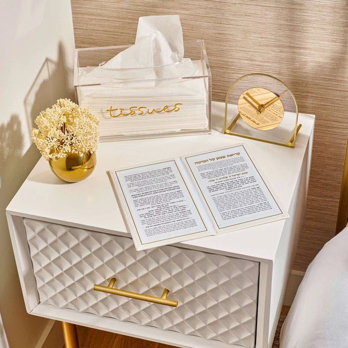 Leather Kriyas Shema prayer book in tan displayed on white nightstand with prayer cards and gold home decor accessories.