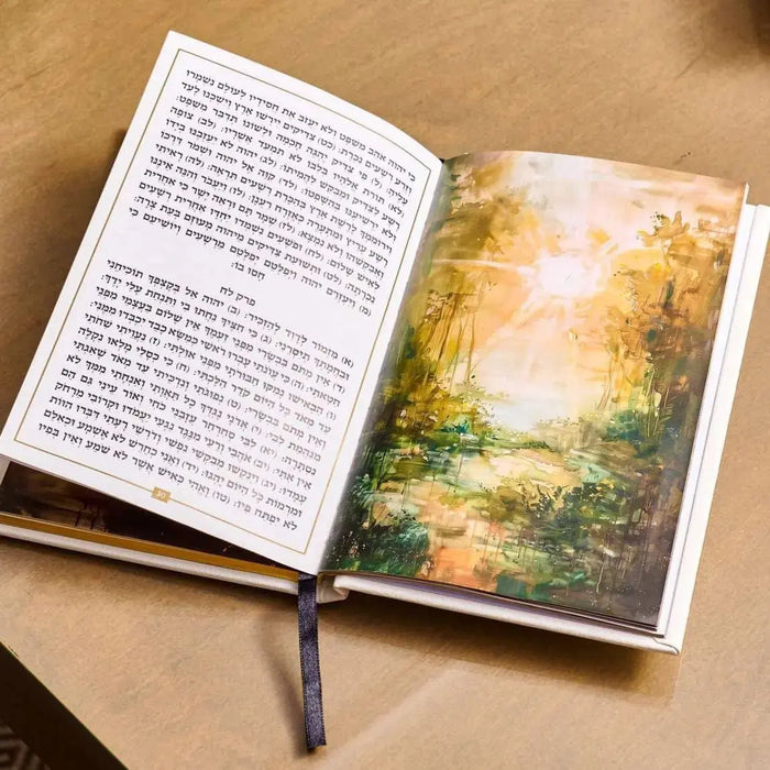 Open leather-bound Tehillim book with painted landscape artwork on right page, showing gold and green tones, displayed on tan surface.