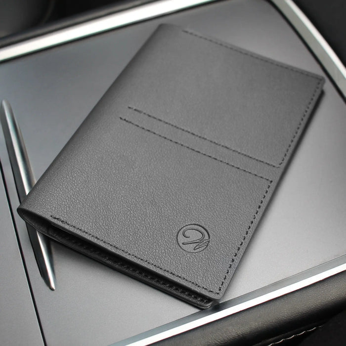 Black leather passport case by Waterdale Collection displayed on white surface with pen, featuring compact design with card slot detail.
