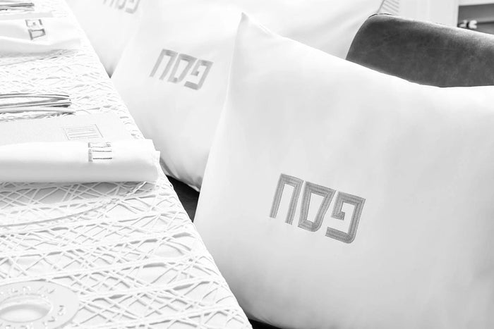 Two leather pillow cases in silver and gold displayed on white bedding and architectural blueprints, showcasing the luxe metallic finishes.