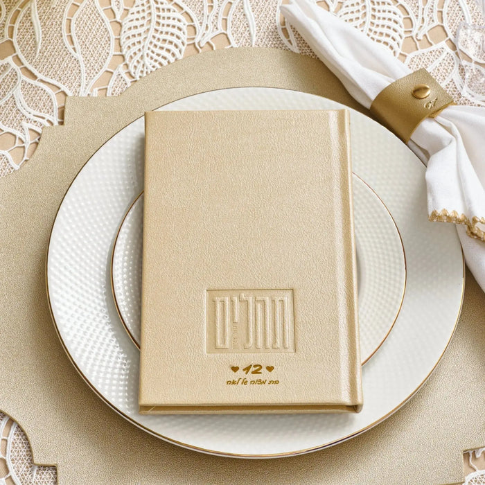 Cream hardcover personalized book with embossed monogram on cover, displayed on white plate with beige napkin and striped tie in elegant table setting.