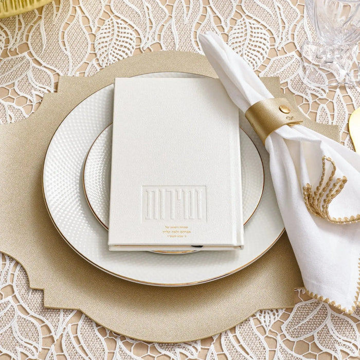 White personalized hardcover book displayed on stacked cream plates with linen napkin and twine bow on textured beige tablecloth.