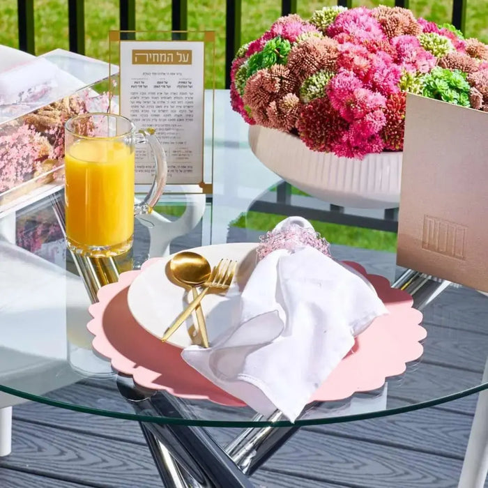 Rose leather scalloped charger plate by Waterdale Collection displayed on a styled table setting with pink flowers and orange juice.
