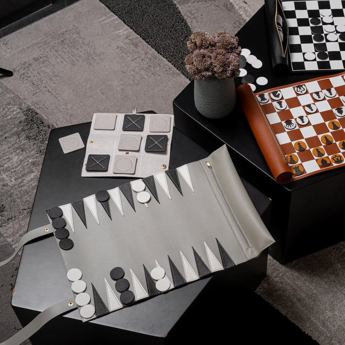 Black and white leather tic tac toe game set displayed with pieces and board on gray surface, showing classic game design.