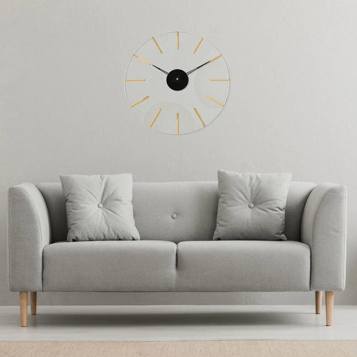 Gold Line Clock by Waterdale Collection featuring minimalist design with thin rays around black center, mounted above gray sofa with pillows.
