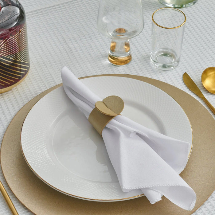Gold leather loop napkin wrap holding a white napkin on a place setting with gold charger plate and glassware
