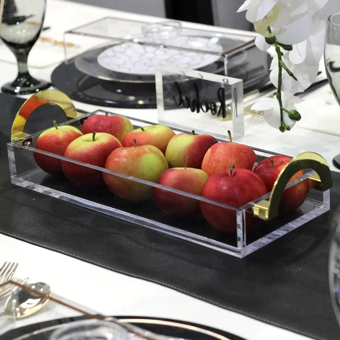 Clear acrylic luxury bread tray filled with colorful apples, featuring sleek black handles and metal accents on dark countertop.