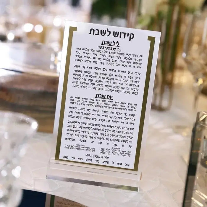 Gold and silver lucite Kiddush card by Waterdale Collection with Hebrew text, displayed in clear acrylic stand for Shabbat.