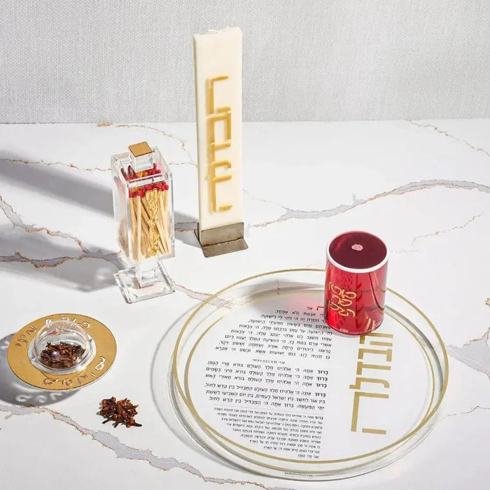 Minimalist Havdalah set with gold accents featuring spice box, candle, wine cup, and prayer book on white surface