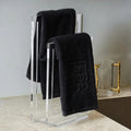 Embossed netilas yadayim towel set displayed on modern metal stand with three folded towels and decorative gold item on shelf.