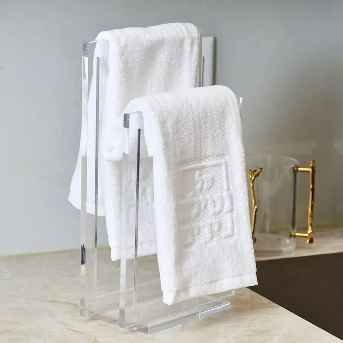 Modern clear acrylic finger towel stand holding white folded towels, displayed on marble counter with gold bathroom accessories