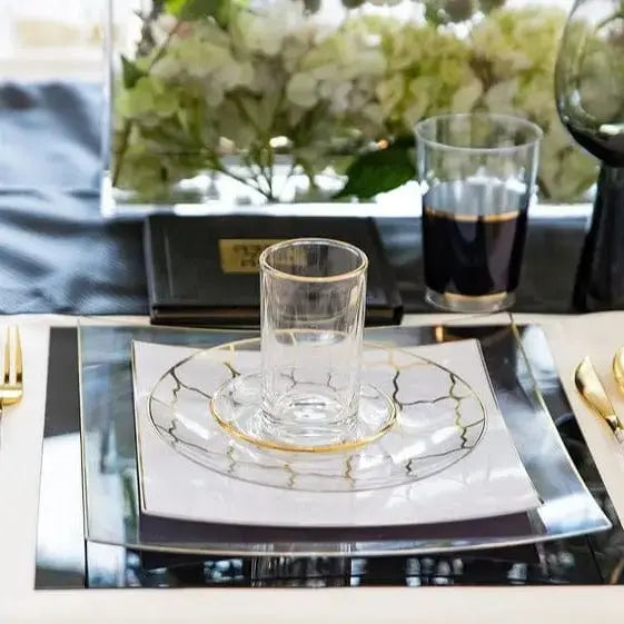 Modern glass Kiddush cups with geometric designs arranged on a table setting with dark napkins and fresh greenery, perfect for Pesach celebrations.
