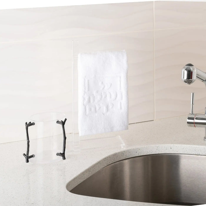 White embossed Netilas Yadayim finger towel displayed on bathroom vanity near sink, featuring decorative raised pattern design for hand washing.